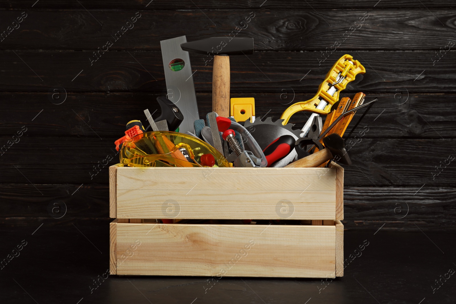 Photo of Wooden crate with different carpenter's tools on black table