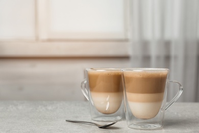 Glass cups of tasty caramel macchiato and spoon on table, space for text