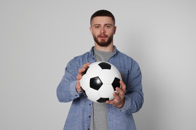 Athletic young man with soccer ball on light grey background, selective focus