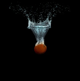 Tangerine falling down into clear water against black background