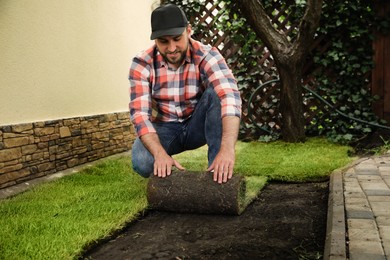 Photo of Young man laying grass sod on ground at backyard