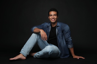 Handsome young African-American man sitting on black background