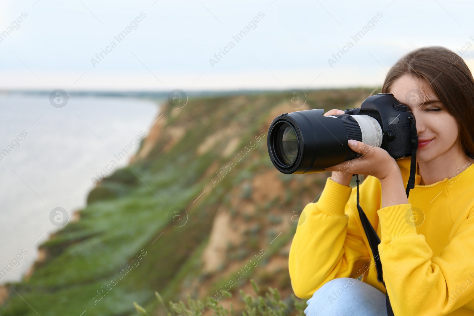 Photo of Female photographer taking picture of beautiful landscape with professional camera on green hill. Space for text