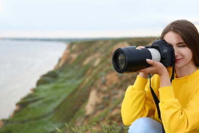 Female photographer taking picture of beautiful landscape with professional camera on green hill. Space for text