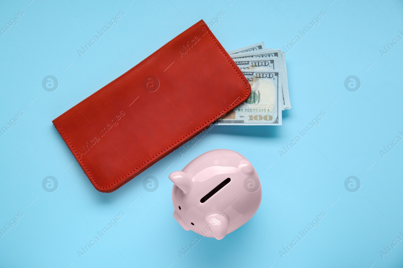 Photo of Piggy bank and wallet with banknotes on light blue background, flat lay