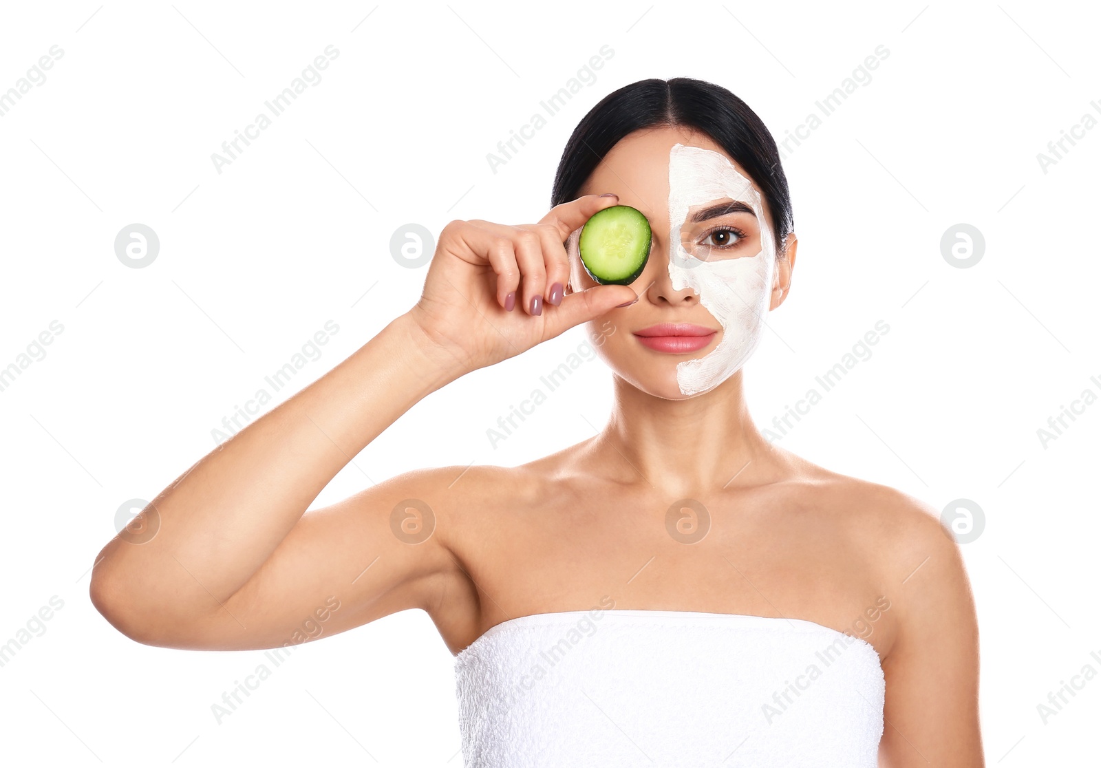 Photo of Young woman with cleansing mask applied on half of face holding cucumber against white background