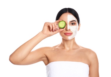 Young woman with cleansing mask applied on half of face holding cucumber against white background