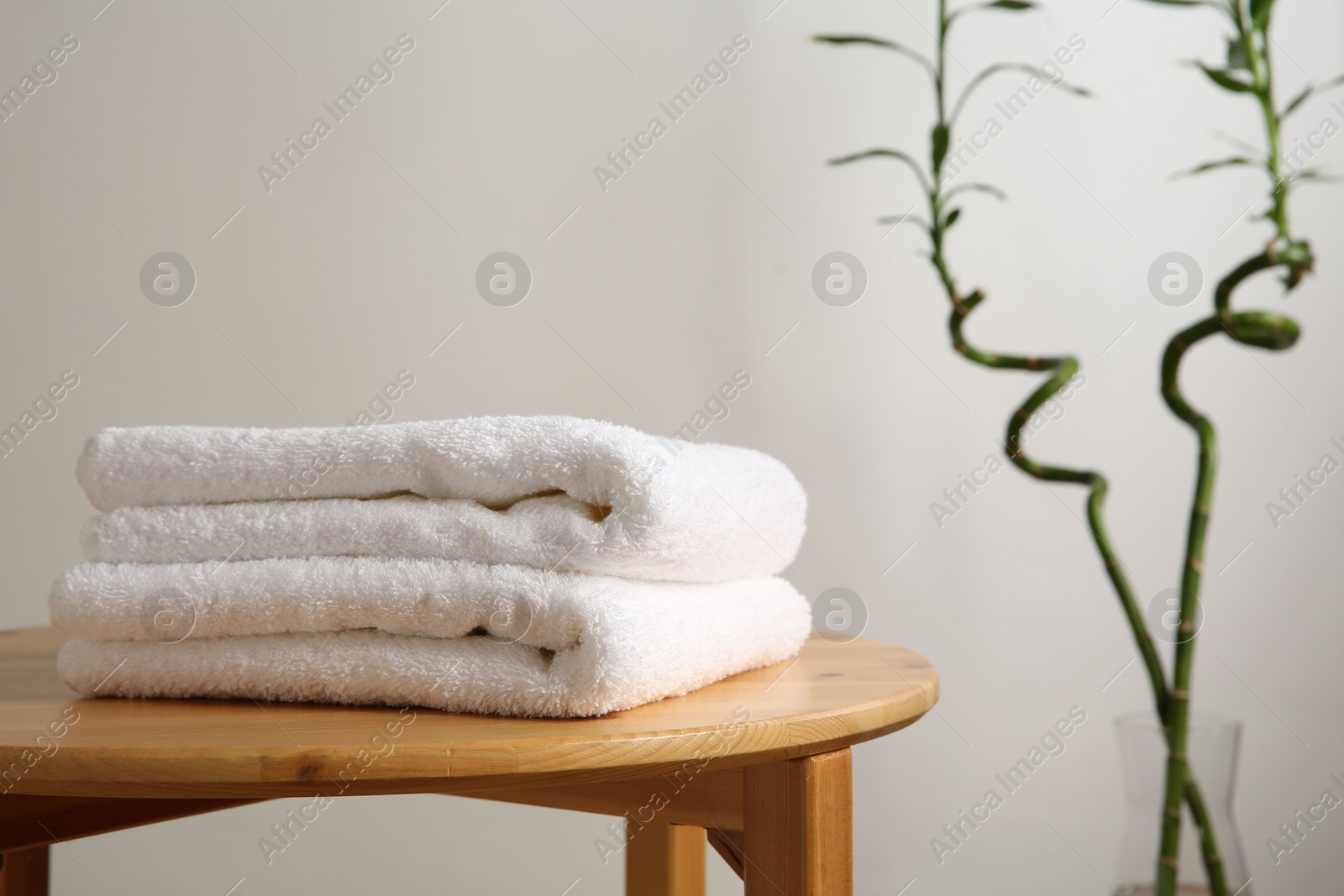 Photo of Folded towels on stool against white wall, closeup. Space for text