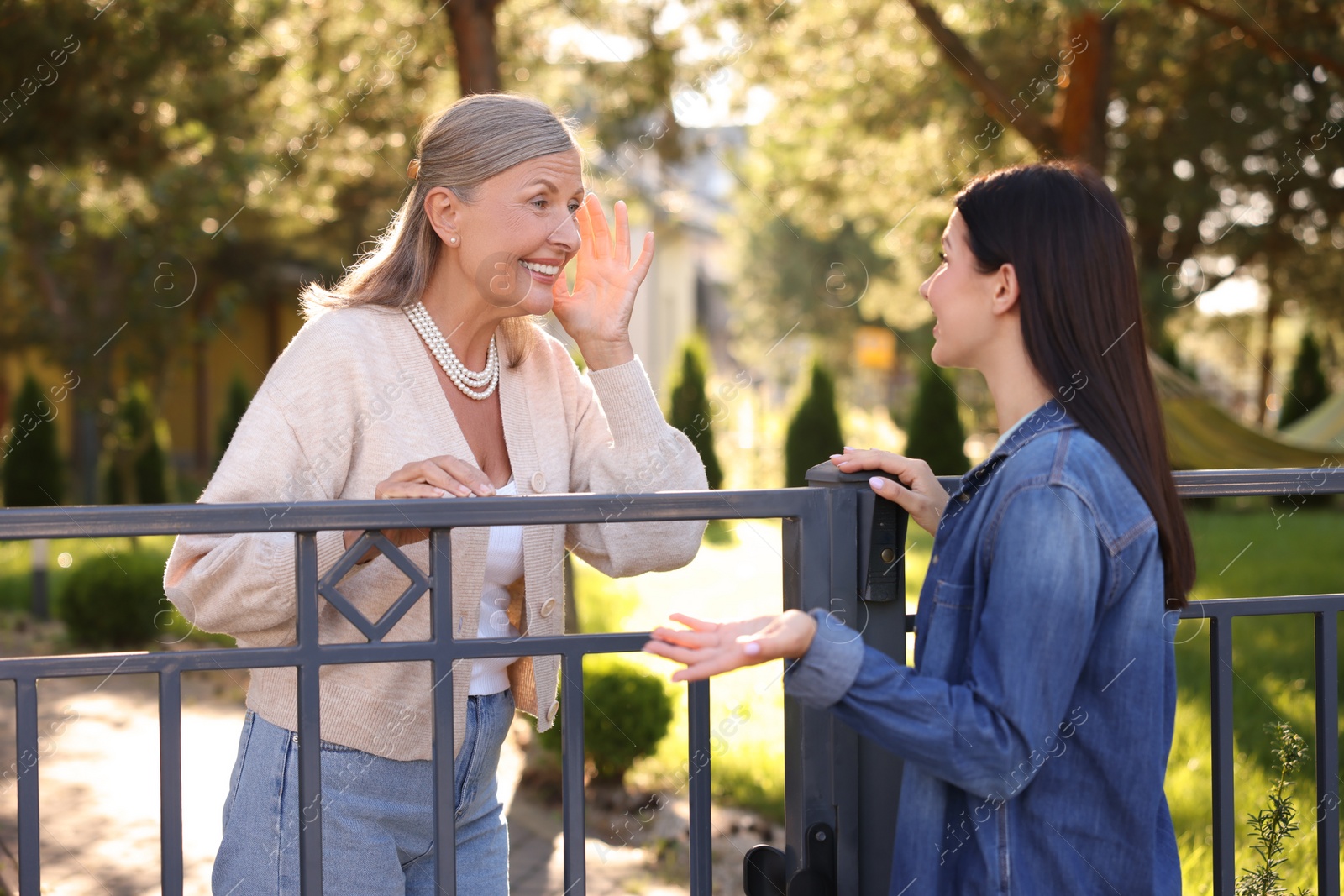 Photo of Friendly relationship with neighbours. Happy women talking near fence outdoors