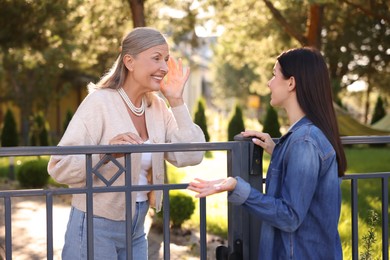 Photo of Friendly relationship with neighbours. Happy women talking near fence outdoors