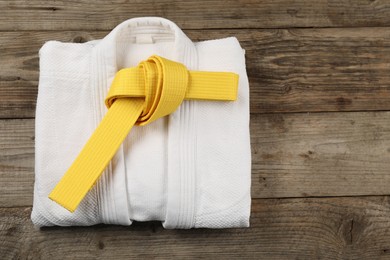 Yellow karate belt and white kimono on wooden background, top view. Space for text