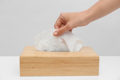 Woman taking paper tissue from holder on light background, closeup