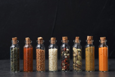 Glass bottles with different spices on table against black background