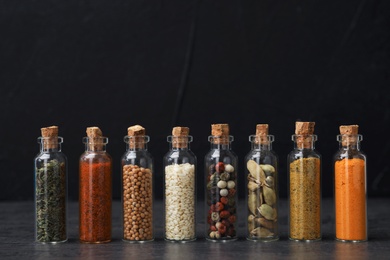 Photo of Glass bottles with different spices on table against black background