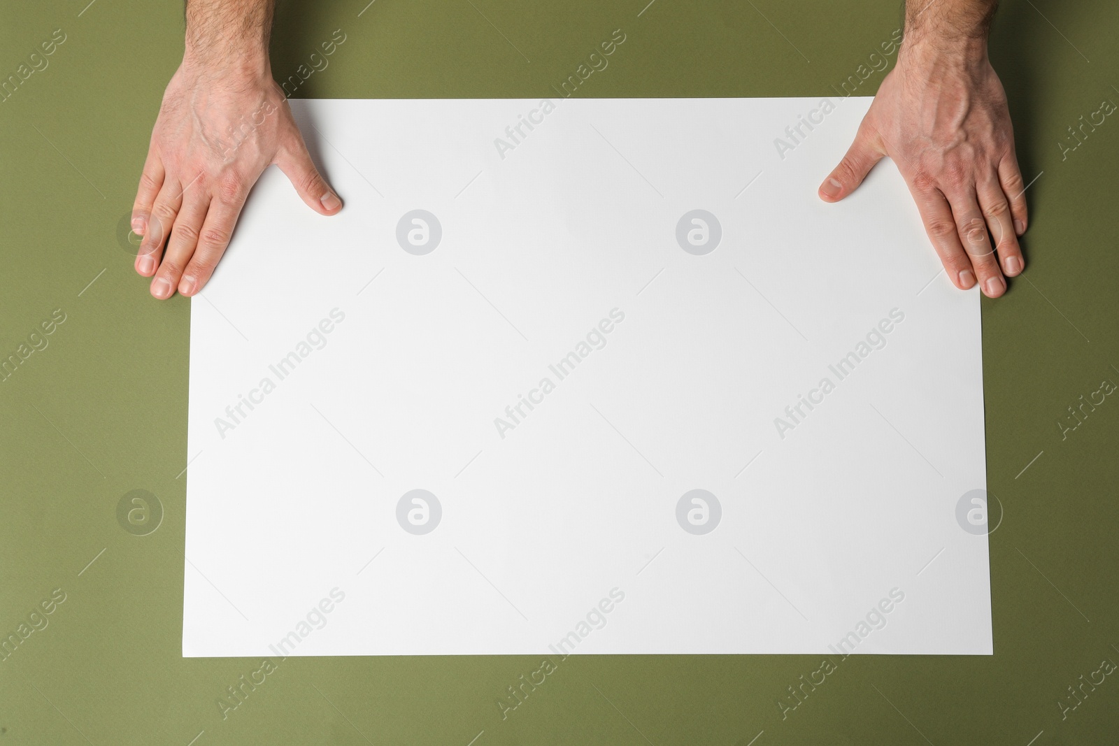 Photo of Man with empty sheet of paper on olive background, top view. Mockup for design