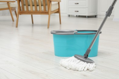 Photo of Mop and bucket on white parquet indoors, space for text. Cleaning floor