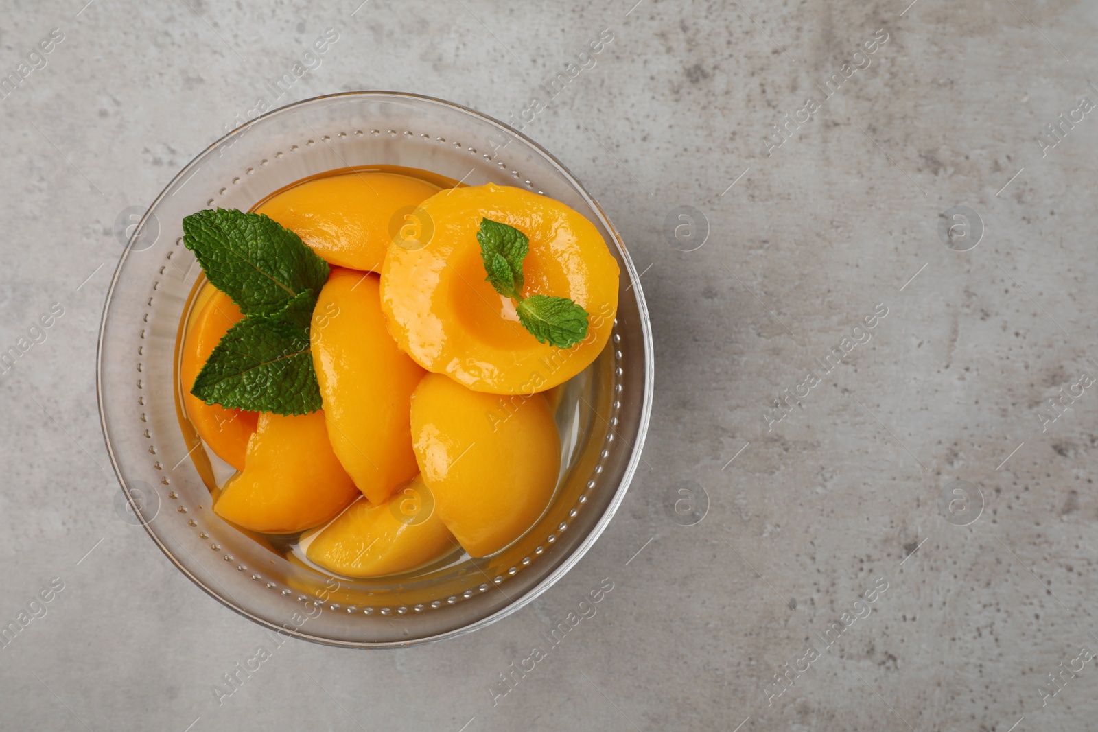 Photo of Canned peach halves in glass bowl on light grey table, top view. Space for text