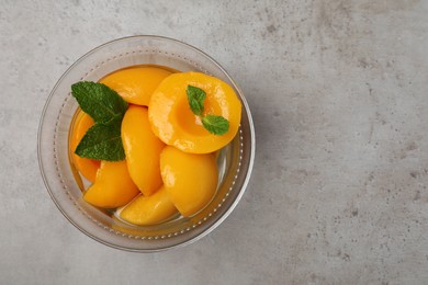 Canned peach halves in glass bowl on light grey table, top view. Space for text