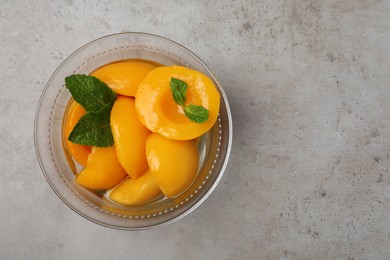 Photo of Canned peach halves in glass bowl on light grey table, top view. Space for text