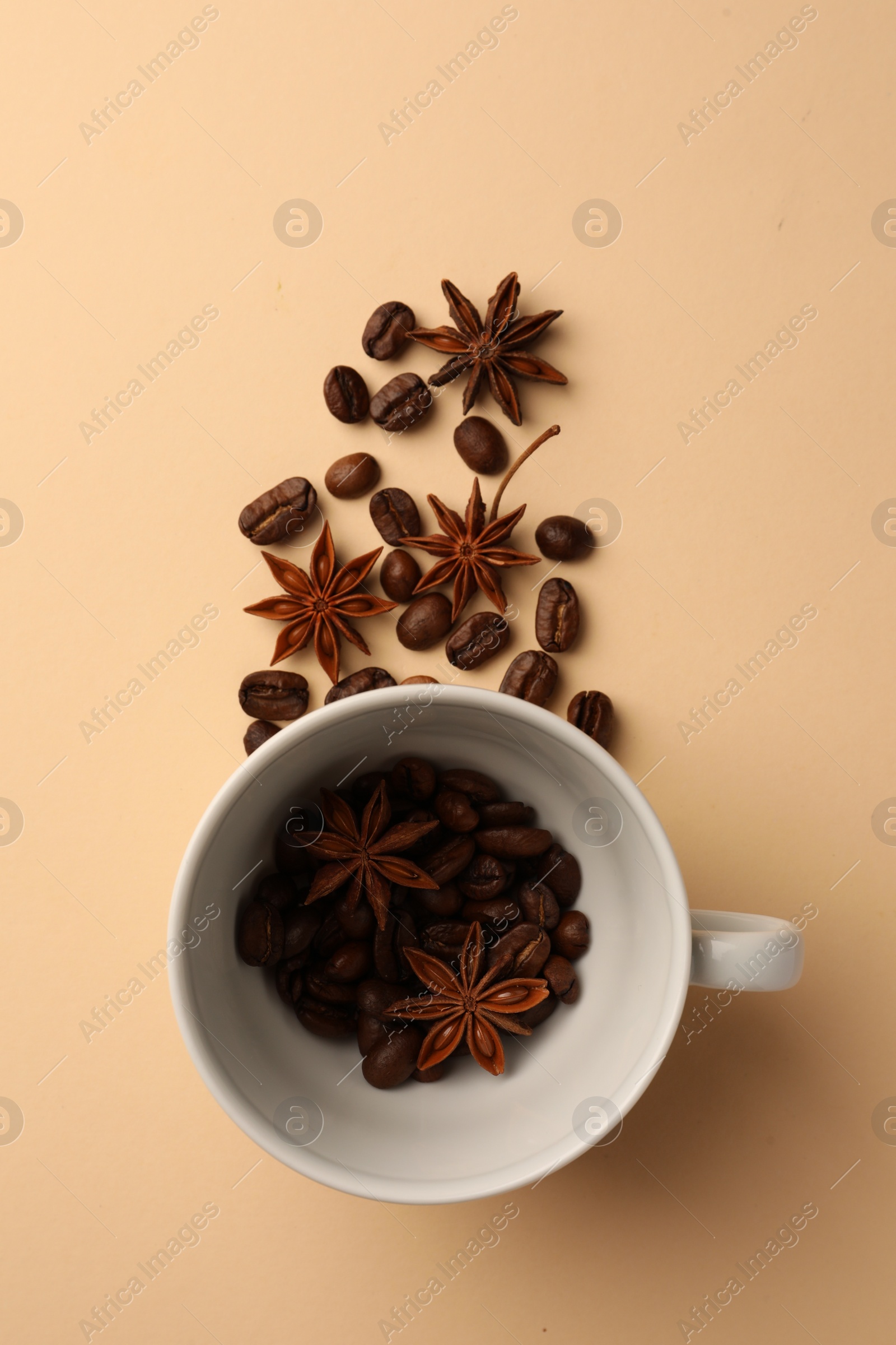 Photo of Cup with coffee beans and anise stars on beige background, flat lay