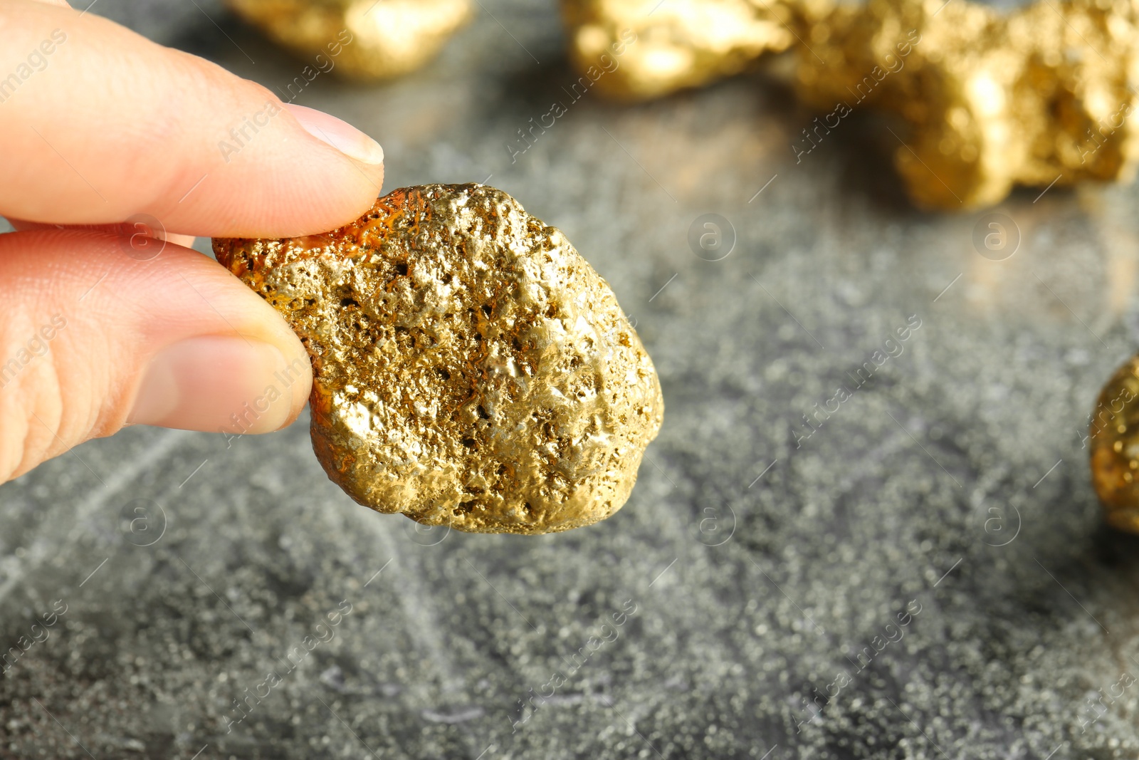 Photo of Woman holding gold nugget at grey textured table, closeup. Space for text