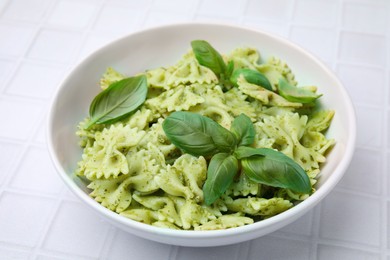 Delicious pasta with pesto sauce and basil on white tiled table, closeup
