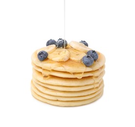 Pouring honey onto delicious pancakes with banana slices and blueberries on white background