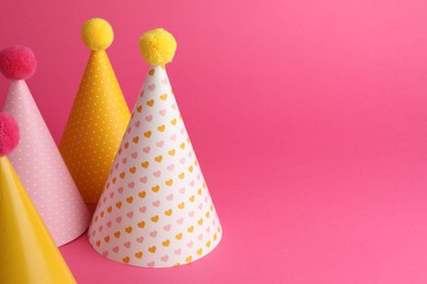 Beautiful party hats with pompoms on pink background, space for text