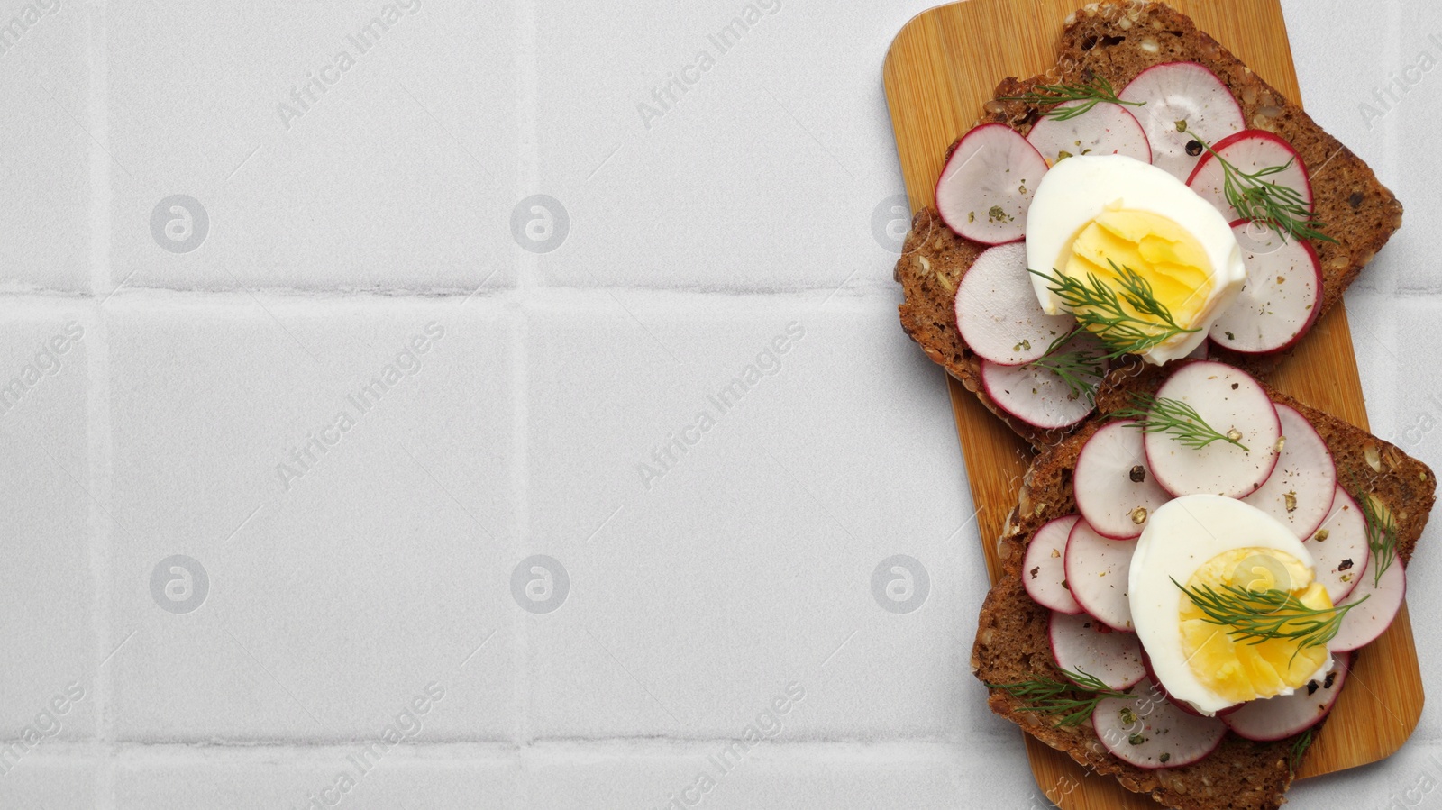 Photo of Tasty sandwiches with boiled egg and radish on white tiled table, top view. Space for text