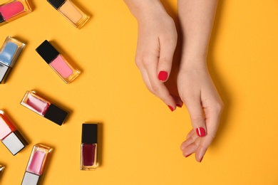 Photo of Woman with red manicure and nail polish bottles on color background, top view