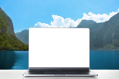Image of Modern laptop with blank screen on white table and view of beautiful mountain landscape and lake