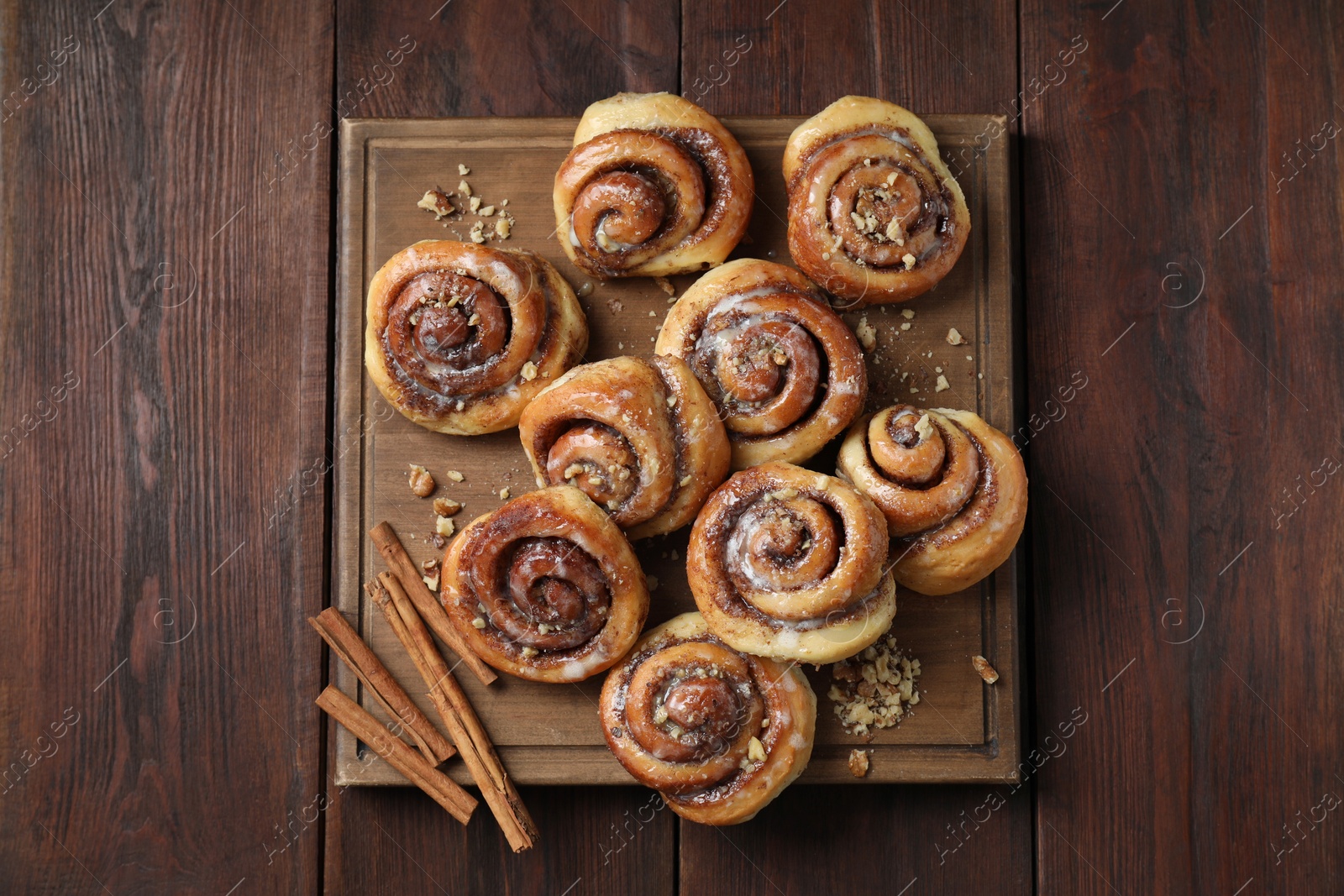 Photo of Tasty cinnamon rolls, sticks and nuts on wooden table, top view