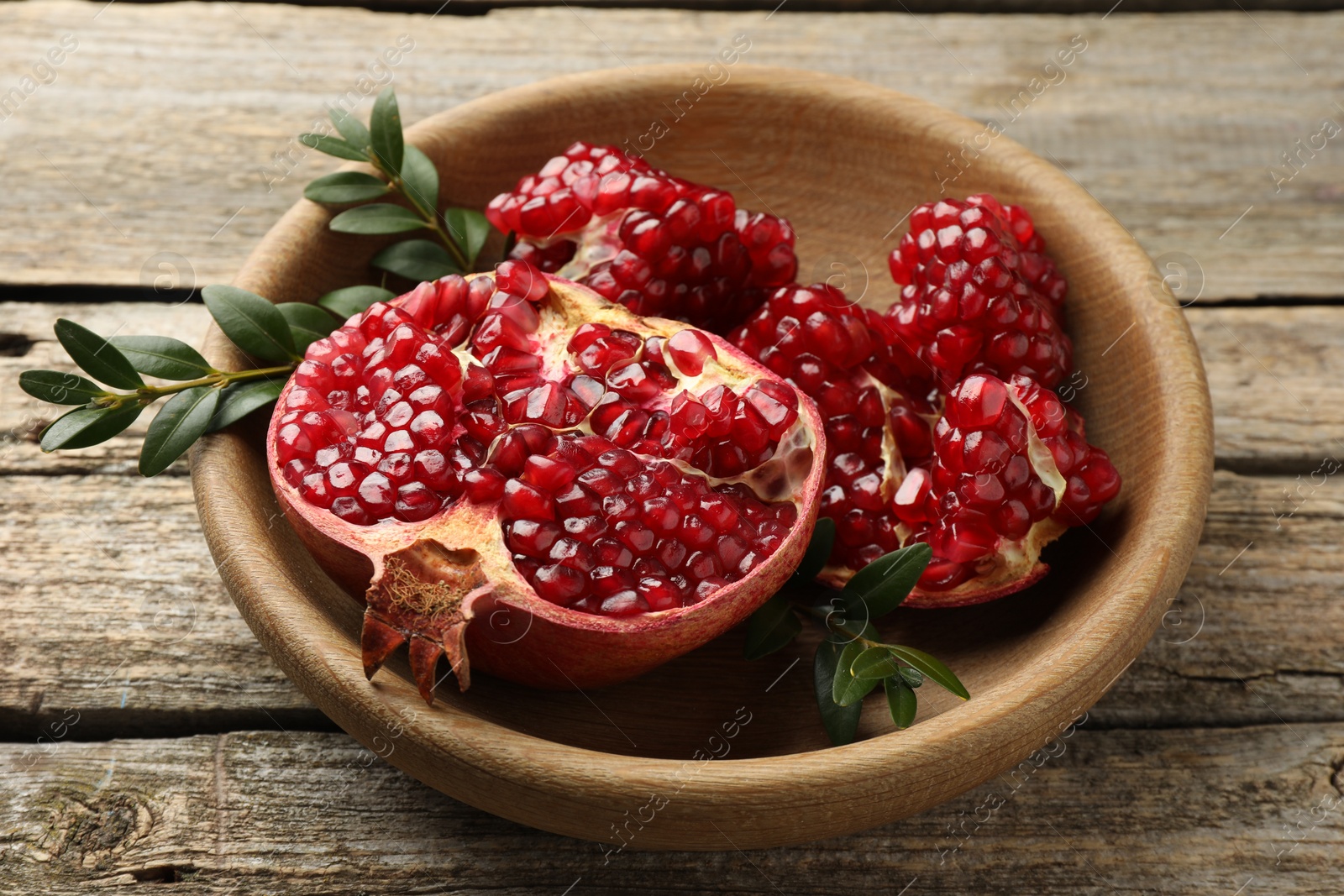 Photo of Cut fresh pomegranate and green leaves on wooden table, closeup