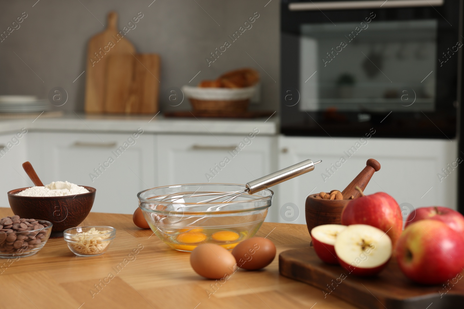 Photo of Cooking process. Metal whisk, bowl and products on wooden table in kitchen