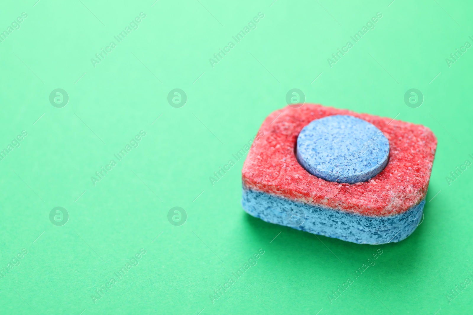 Photo of Dishwasher detergent tablet on green background, closeup. Space for text