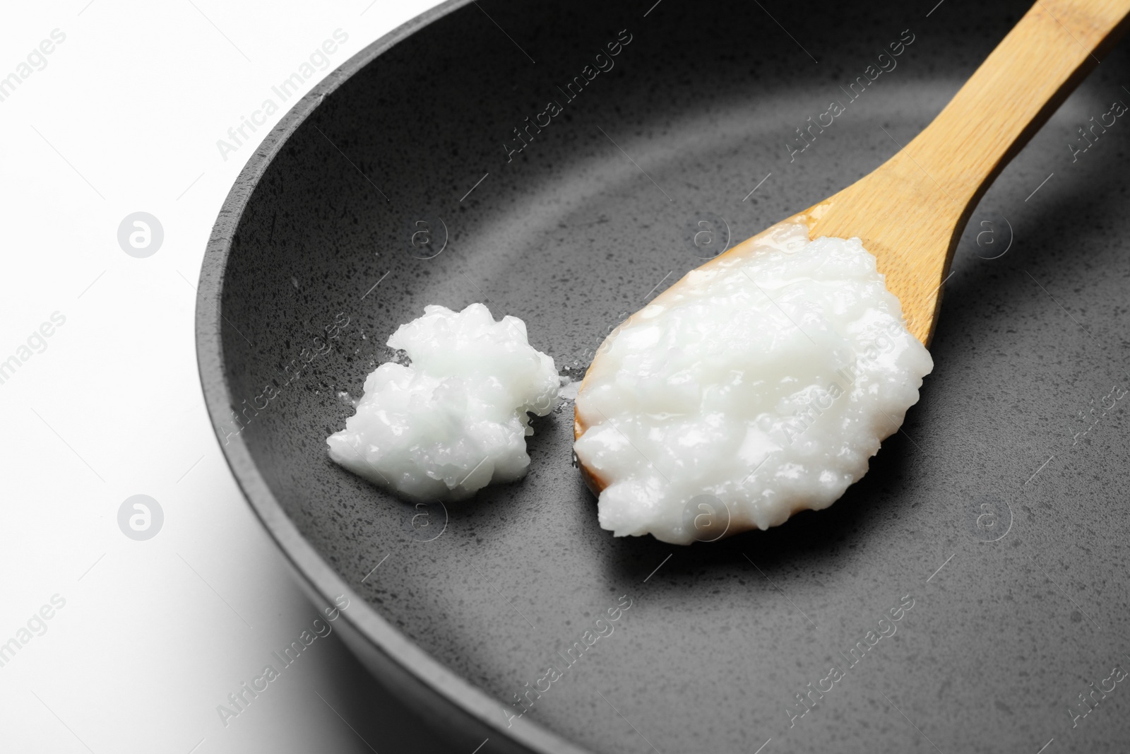 Photo of Frying pan with coconut oil and wooden spoon on white background, closeup. Healthy cooking