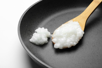 Photo of Frying pan with coconut oil and wooden spoon on white background, closeup. Healthy cooking