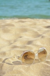 Photo of Stylish sunglasses on sandy beach near sea