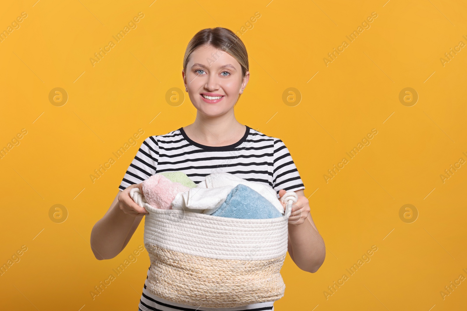 Photo of Happy woman with basket full of laundry on orange background