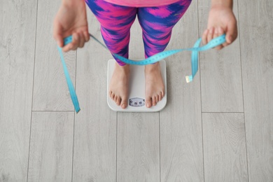 Photo of Woman with tape measuring her weight using scales on floor, top view. Healthy diet