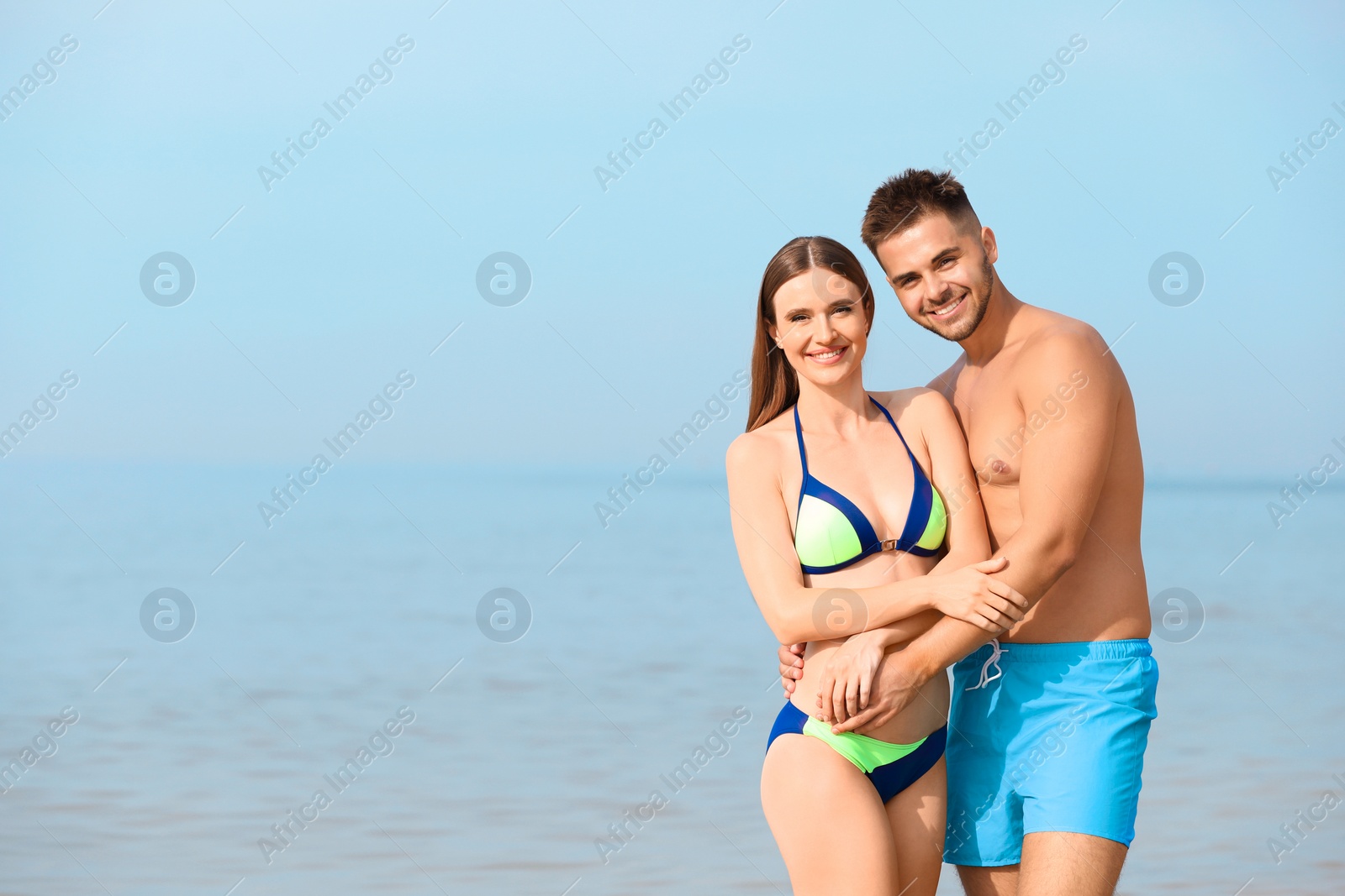 Photo of Young woman in bikini with her boyfriend on beach, space for text. Lovely couple