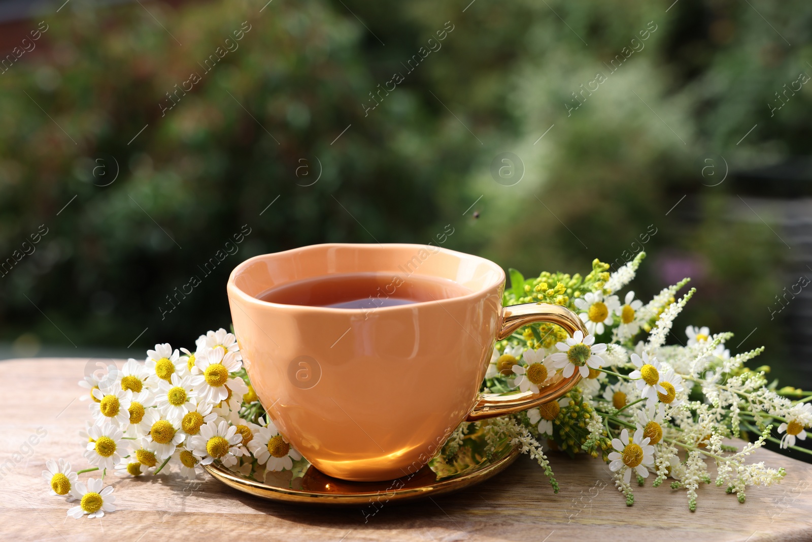 Photo of Cup of delicious chamomile tea and fresh flowers outdoors on sunny day