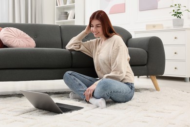Photo of Happy woman with laptop on rug in living room