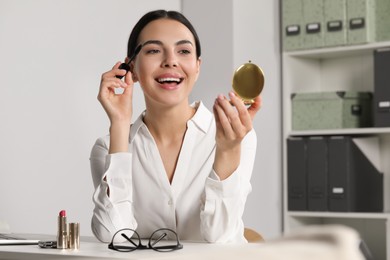 Young woman using cosmetic pocket mirror while applying makeup indoors