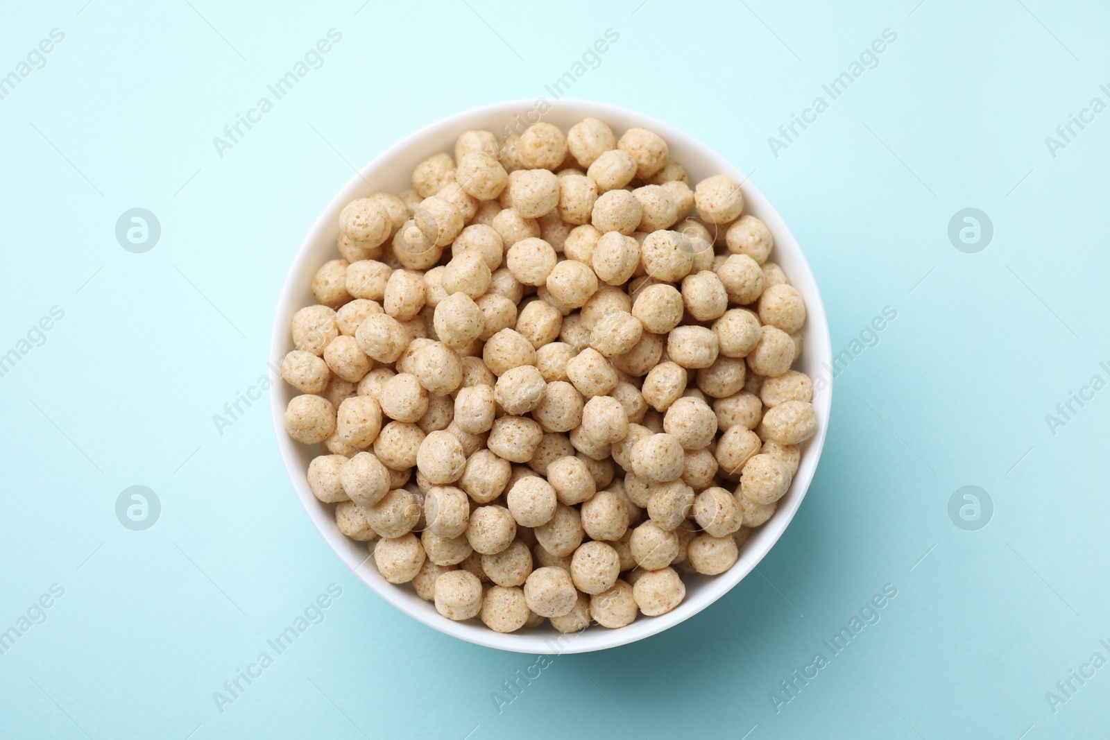 Photo of Tasty cereal balls in bowl on light blue table, top view