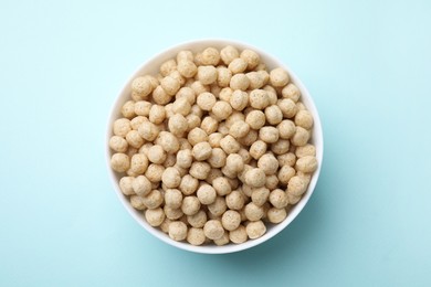 Photo of Tasty cereal balls in bowl on light blue table, top view