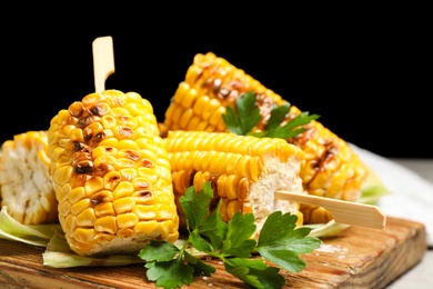 Photo of Tasty grilled corn cobs on wooden board, closeup