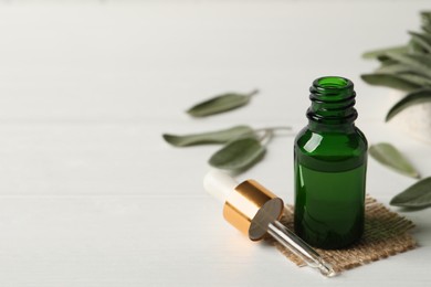 Bottle of essential sage oil, dropper and leaves on white table. Space for text