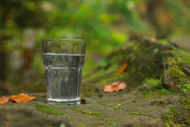 Glass of fresh water on stone with moss in forest. Space for text