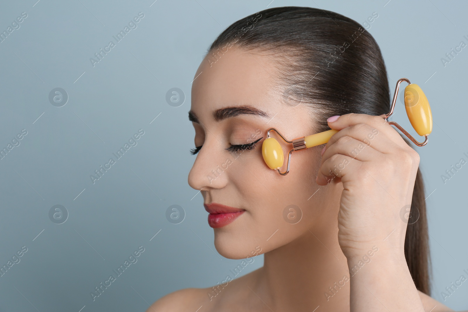 Photo of Woman using natural jade face roller on grey background, space for text